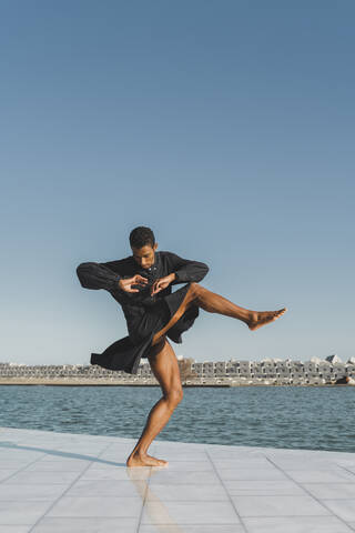 Young man wearing black kaftan performing at the waterfront stock photo