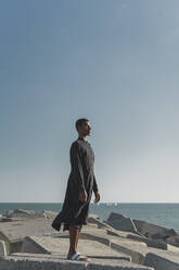 Young man standing at the coast wearing black kaftan - AFVF05208