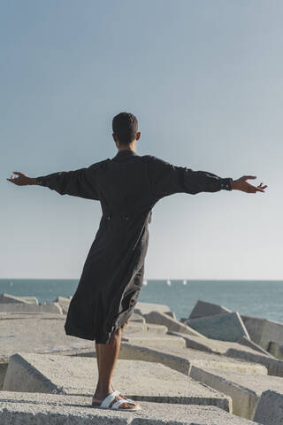 Young man wearing black kaftan on concrete blocks at the coast stock photo