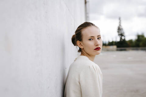 Porträt einer ernsten jungen Frau mit roten Lippen, die sich an eine Wand lehnt, lizenzfreies Stockfoto