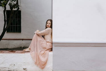 Porträt einer melancholischen jungen Frau, die barfuß an einer Wand sitzt - TCEF00068
