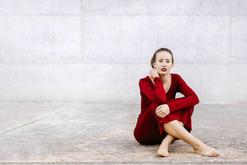 Porträt einer barfüßigen jungen Frau im roten Kleid, die im Freien auf dem Boden sitzt - TCEF00074