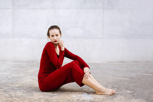 Porträt einer barfüßigen jungen Frau im roten Kleid, die im Freien auf dem Boden sitzt - TCEF00075