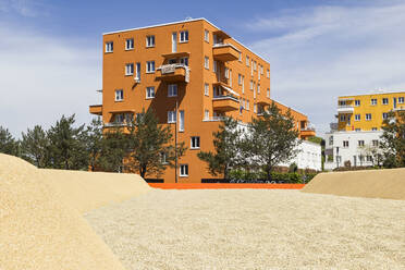 Germany, Bavaria, Munich, Sandy playground in front of orange painted residential building - MAMF01046