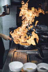 Chef preparing a flambe dish at gas stove in restaurant kitchen - OCAF00436