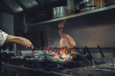 Chef preparing a flambe dish at gas stove in restaurant kitchen - OCAF00437