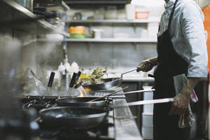 Chef preparing a dish at gas stove in restaurant kitchen - OCAF00442