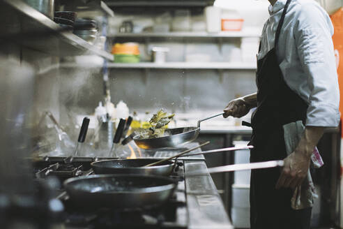Koch bei der Zubereitung eines Gerichts am Gasherd in einer Restaurantküche - OCAF00442