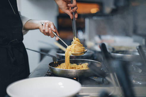 Chef preparing a pasta dish in traditional Italian restaurant kitchen - OCAF00446