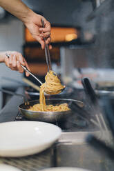 Chef preparing a pasta dish in traditional Italian restaurant kitchen - OCAF00448
