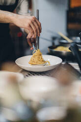 Chef preparing a pasta dish in traditional Italian restaurant kitchen - OCAF00449