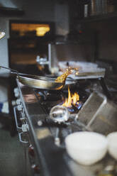 Preparing a dish at gas stove in restaurant kitchen - OCAF00458