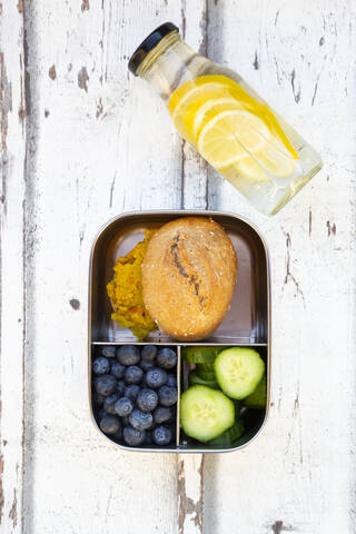 Eine Flasche Limonade und eine Lunchbox mit Gurkenscheiben, Blaubeeren und Brötchen mit Linsenpaste, lizenzfreies Stockfoto