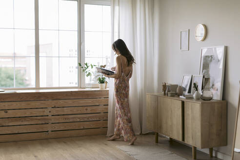 Young woman at the window at home holding a book - JPF00412