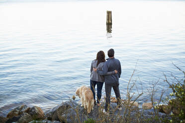 Affectionate couple with dog hugging, enjoying lake view - FSIF04554