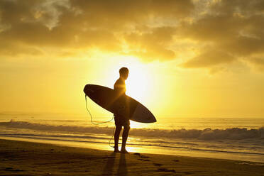 Silhouettierter männlicher Surfer mit Surfbrett am ruhigen Strand bei Sonnenuntergang - FSIF04569