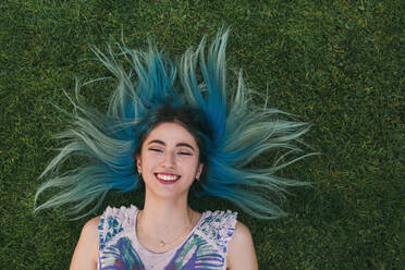 Overhead portrait carefree young woman with blue hair laying in grass - FSIF04576