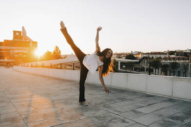 Playful young female dancer doing standing splits in sunny city park - FSIF04599