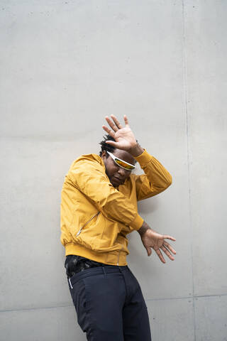 Älterer Mann mit verspiegelter Sonnenbrille und gelber Jacke hebt die Hände, lizenzfreies Stockfoto