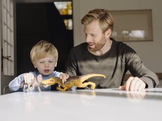 Father and son playing with dinosaur figures at home - KNSF07002