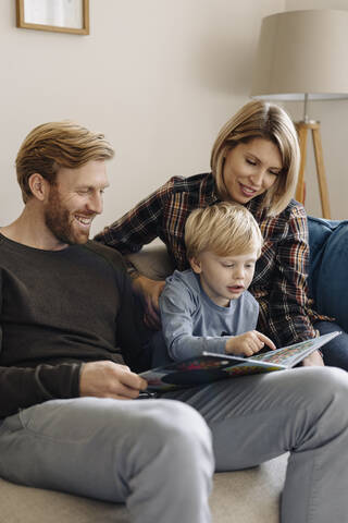 Familie schaut sich auf der Couch zu Hause ein Buch an, lizenzfreies Stockfoto