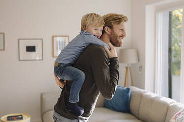 Happy father carrying son piggyback at home - KNSF07012