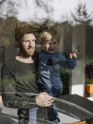 Father and son looking out of window at home - KNSF07023