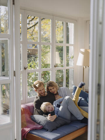 Glückliche Familie benutzt Mobiltelefon im Sonnenzimmer zu Hause, lizenzfreies Stockfoto