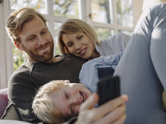 Happy family using cell phone in sunroom at home - KNSF07030