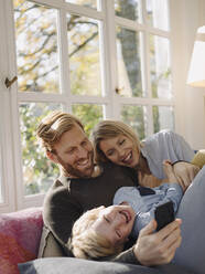 Glückliche Familie benutzt Mobiltelefon im Sonnenzimmer zu Hause - KNSF07031