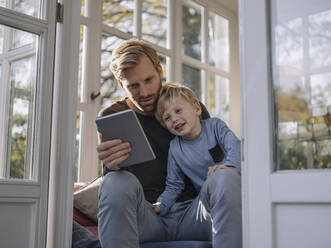 Vater und Sohn benutzen ein Tablet im Sonnenzimmer zu Hause - KNSF07039