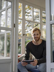 Porträt eines Mannes, der ein Tablet im Sonnenzimmer zu Hause benutzt - KNSF07041