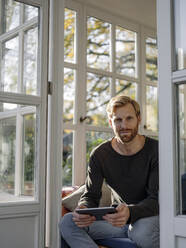 Portrait of man using tablet in sunroom at home - KNSF07041