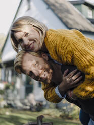 Portait of happy man giving his wife a piggyback ride in garden - KNSF07051
