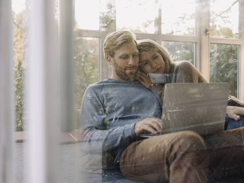 Man with wife using laptop in sunroom at home stock photo