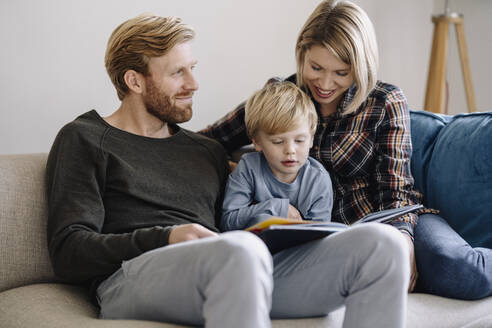 Familie schaut sich auf der Couch zu Hause ein Buch an - KNSF07069