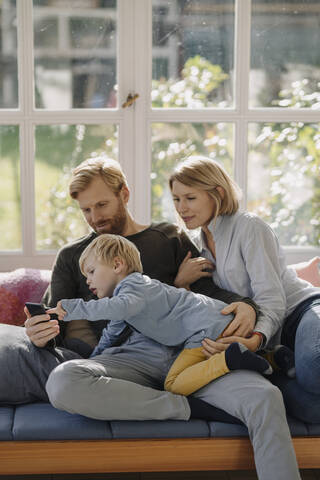 Familie benutzt Mobiltelefon im Wintergarten zu Hause, lizenzfreies Stockfoto