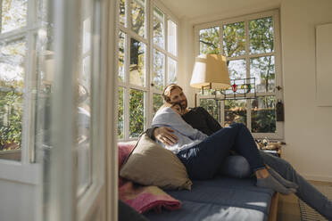 Affectionate couple relaxing in sunroom at home - KNSF07080
