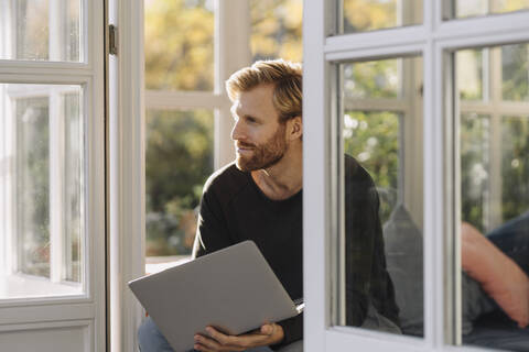 Mann benutzt Laptop im Sonnenzimmer zu Hause, lizenzfreies Stockfoto