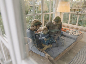Little boy with parents unwrapping gift in sunroom at home - KNSF07104