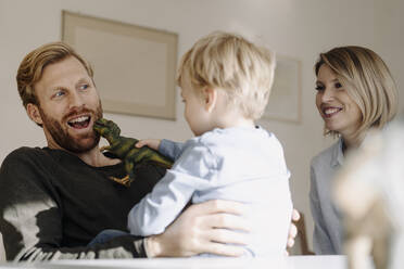 Happy family playing with dinosaur figure at home - KNSF07107