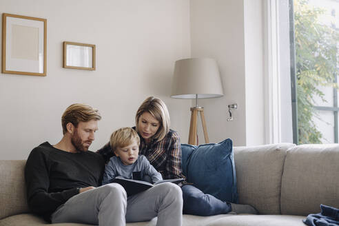 Familie schaut sich auf der Couch zu Hause ein Buch an - KNSF07108