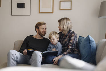 Familie schaut sich auf der Couch zu Hause ein Buch an - KNSF07109