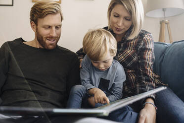 Familie schaut sich auf der Couch zu Hause ein Buch an - KNSF07110
