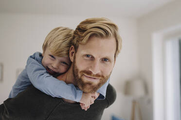 Porträt eines lächelnden Vaters, der seinen Sohn zu Hause huckepack trägt - KNSF07114