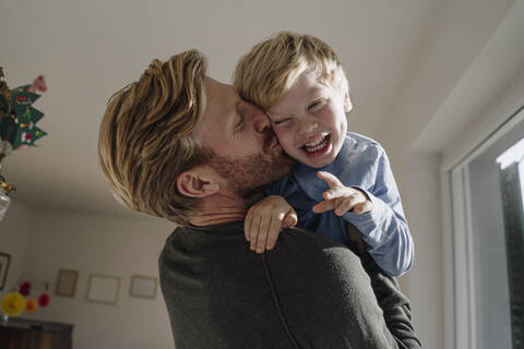 Father carrying and kissing son at home stock photo