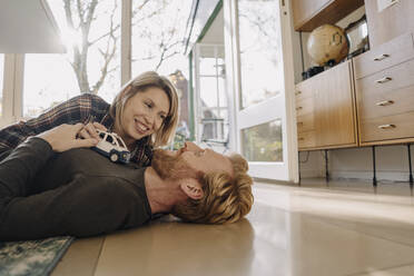 Happy couple lying on the floor at home with toy car - KNSF07125