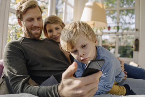 Glückliche Familie benutzt Mobiltelefon im Sonnenzimmer zu Hause - KNSF07127