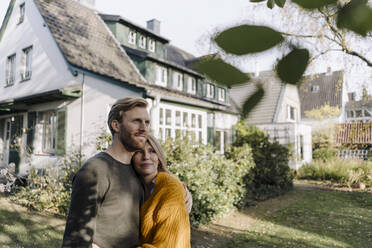 Lächelndes Paar, das sich im Garten seines Hauses umarmt - KNSF07131