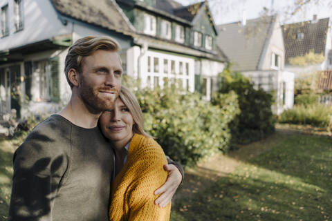 Lächelndes Paar, das sich im Garten seines Hauses umarmt, lizenzfreies Stockfoto